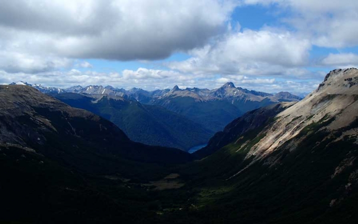 A vast mountainous landscape appears blue in the distance under a blue sky dotted with white clouds. 